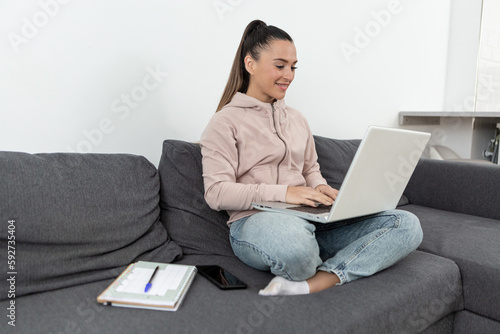 Smiling young woman sitting on sofa using laptop computer