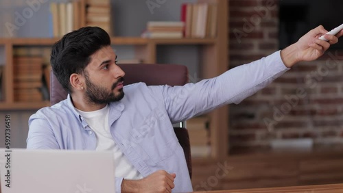 man gets cold and turns on the AC system in a modern office workplace interior. Comfort concept. turn on remote control changing temperature on air conditioner