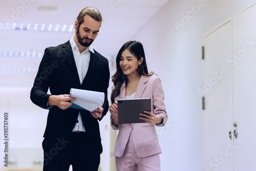 Diverse friend partners colleagues talking walking in modern office hallway. Confident business partners walking down in office building and talking. Professional business people walking and talking