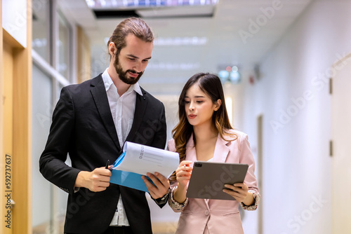 Diverse friend partners colleagues talking walking in modern office hallway. Confident business partners walking down in office building and talking. Professional business people walking and talking