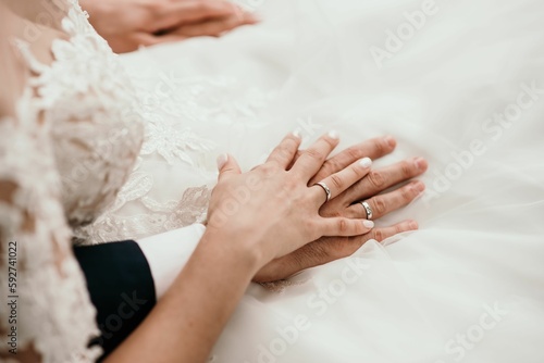 Hands of the groom and bridge with rings on the white wedding dress © Stefan Radosavljevic/Wirestock Creators