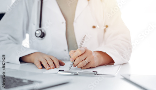 Unknown doctor woman sitting and writing notes at the desk in clinic or hospital office  close up. Medicine concept
