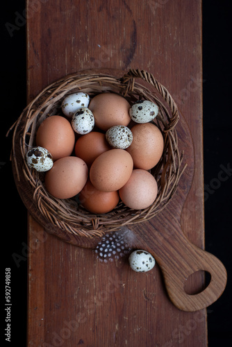 Wicker basket with chicken and quail eggs on a wooden board.
