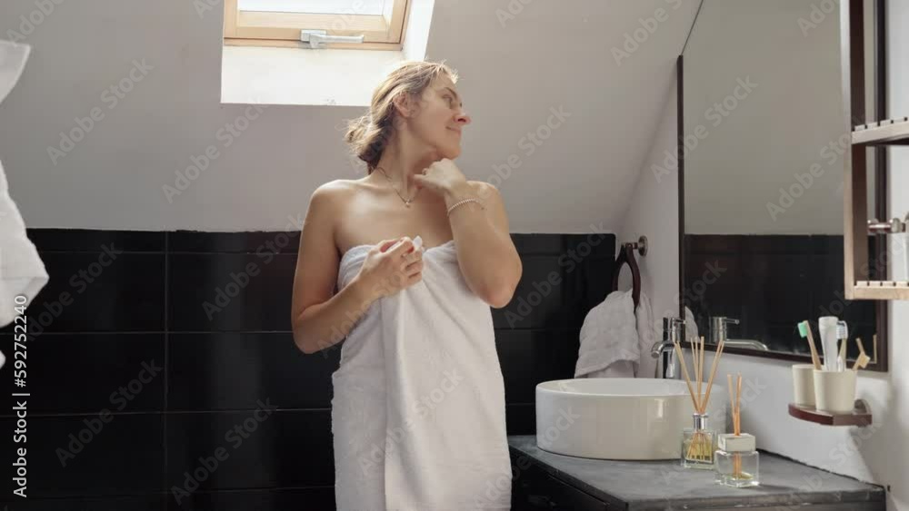 Woman standing in a bath, covered in a towel, and admiring herself in the mirror. Concept of maintaining good hygiene and self-care rituals Woman standing in a bath, covered in a towel, and admiring herself in the mirror. Concept of maintaining good hygiene and self-care rituals