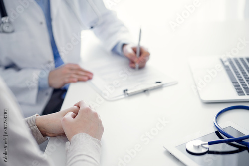 Doctor and patient discussing current health questions while sitting at the table in clinic office, only hands closeup. Medicine concept