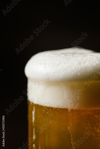 Cold beer with foam in a mug, on a wooden table and a dark background © o_lypa