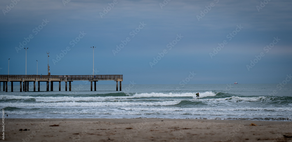 PORT ARANSAS, TX - 9 FEB 2023: Surfer catching a wave on the water of the Gulf of Mexico, near a pier and the beach in evening 