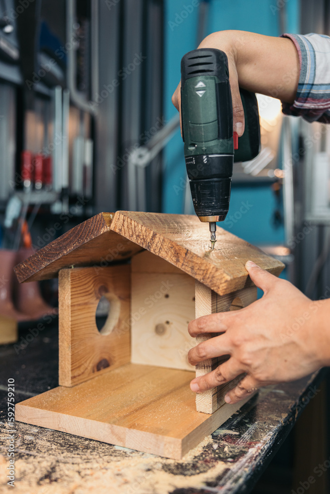 Φωτογραφία Woman's hands screwing with a drill the roof of a birdhouse