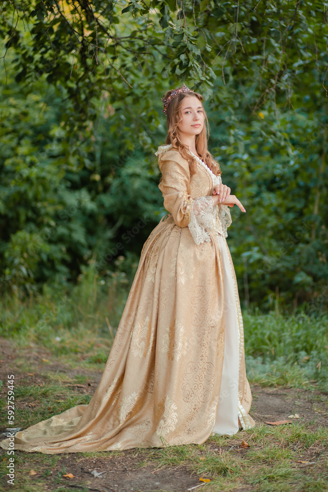 A beautiful young woman in a historical gold dress with a crown. Princess in a medieval dress in the forest.