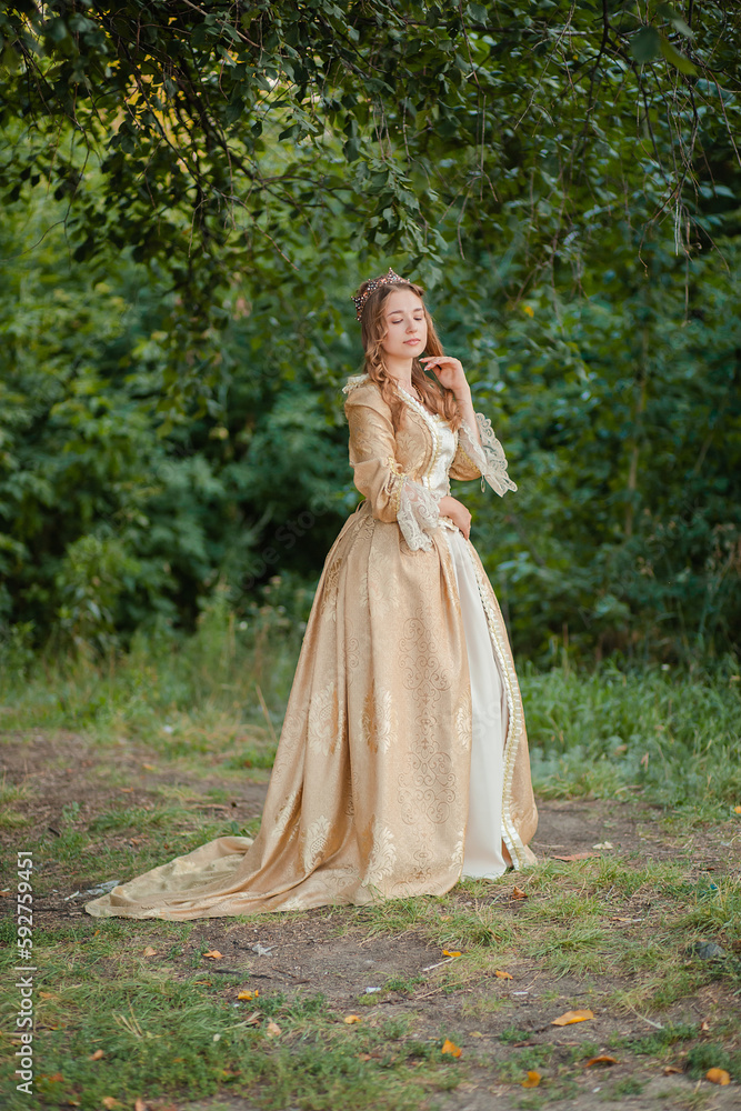 A beautiful young woman in a historical gold dress with a crown. Princess in a medieval dress in the forest. A beautiful young woman in a historical gold dress with a crown. Princess in a medieval dress in the forest.