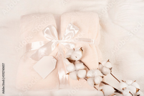 Fototapeta Naklejka Na Ścianę i Meble -  soft surface of a fluffy beige plaid with a mockup sign for an inscription, with a gift ribbon and a branch of cotton. Delicate fluffy plaid in pastel colors, tied with a satin ribbon. gift shop