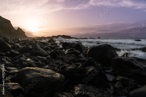 une plage de rochers au pieds de falaises sous un coucher de soleil aux teintes violettes
