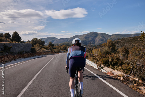 Fototapeta Naklejka Na Ścianę i Meble -  Professional cyclist training on road bike in mountains at sunset. 
Sport background.Fit and athletic man on bicycle. Cyclist in colored cycling kit and helmet. Spain cycling holiday.