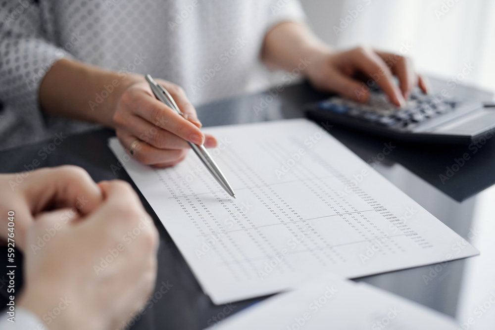 Woman accountant using a calculator and laptop computer while counting and discussing taxes with a client. Business audit and finance concepts Woman accountant using a calculator and laptop computer while counting and discussing taxes with a client. Business audit and finance concepts