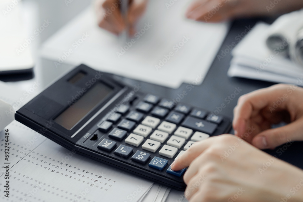 Woman accountant using a calculator and laptop computer while counting taxes for a client. Business audit and finance concepts Woman accountant using a calculator and laptop computer while counting taxes for a client. Business audit and finance concepts