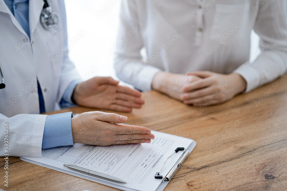 Doctor and patient discussing something while sitting near each other at the wooden desk in clinic, view from above. Medicine concept Doctor and patient discussing something while sitting near each other at the wooden desk in clinic, view from above. Medicine concept