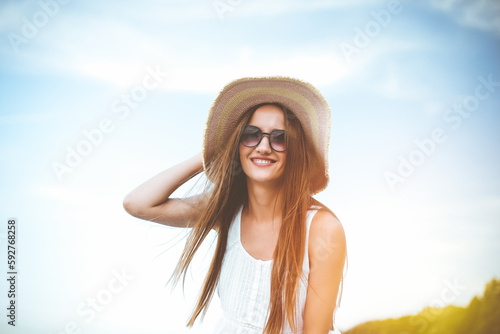 Happy smiling woman in free happiness bliss on ocean beach standing and posing with hat and sunglasses. Portrait of a female model in white summer dress enjoying nature