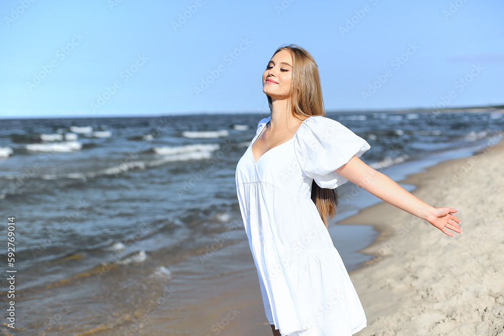 Happy smiling beautiful woman is on the ocean beach in a white summer dress, open arms Happy smiling beautiful woman is on the ocean beach in a white summer dress, open arms