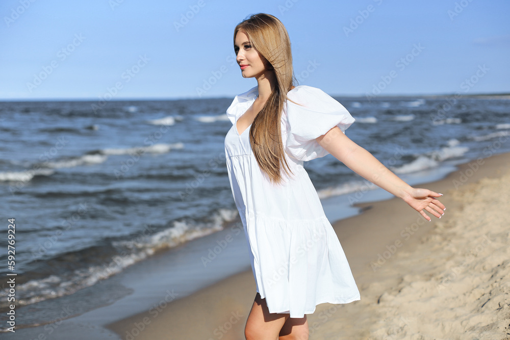 Happy smiling beautiful woman is on the ocean beach in a white summer dress, open arms Happy smiling beautiful woman is on the ocean beach in a white summer dress, open arms