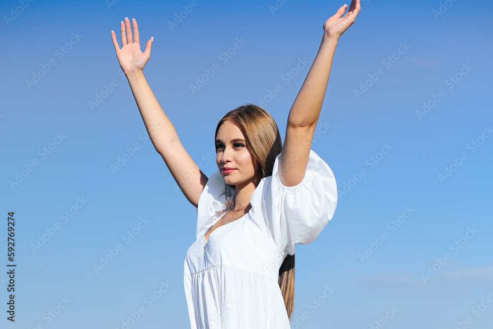 Happy, beautiful woman on the ocean beach standing in a white summer dress, raising hands Happy, beautiful woman on the ocean beach standing in a white summer dress, raising hands
