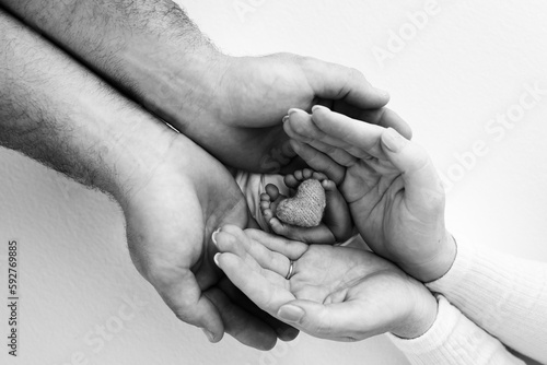 Children's leg in the hands of mother, father, parents. Feet of a tiny newborn close up. Children's leg with a knitted heart. Mom her child. Happy family concept. Black and white photo of motherhood.