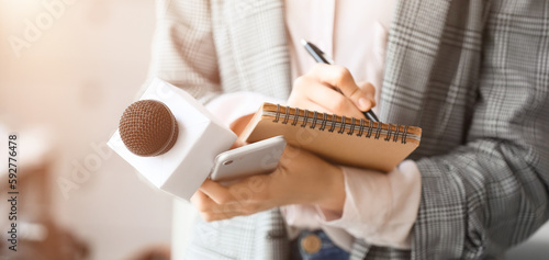 Female journalist with microphone, notebook and phone in office, closeup photo