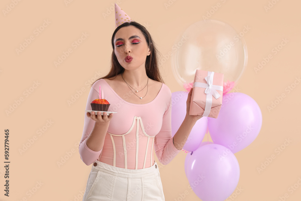 Beautiful woman with cupcake and gift celebrating Birthday on beige background Beautiful woman with cupcake and gift celebrating Birthday on beige background