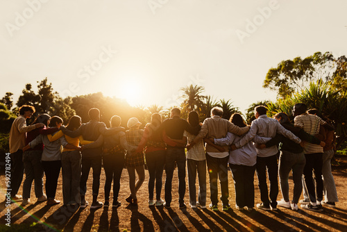 Back view of happy multigenerational people having fun in a public park during sunset time - Community and support concept