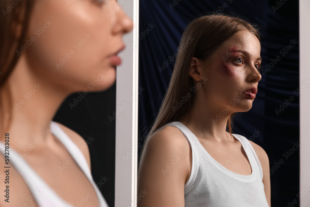 Bruised young woman near mirror on dark background, closeup. Domestic violence concept Bruised young woman near mirror on dark background, closeup. Domestic violence concept