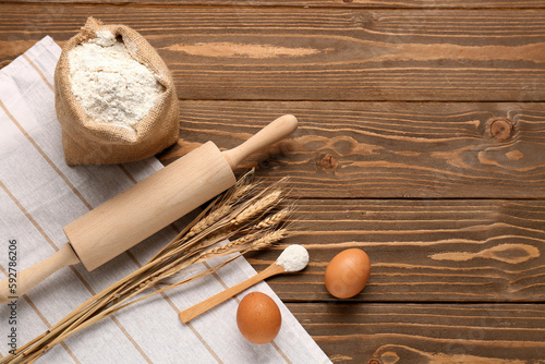 Composition with sack bag of flour, rolling pin, wheat ears and eggs on wooden table