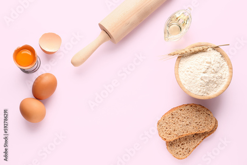Frame made of bowl with wheat flour, bread, eggs and rolling pin on pink background