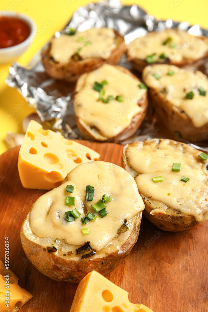 Wooden board with tasty baked potato and cheese, closeup