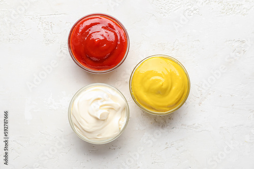 Bowls of ketchup, mayonnaise and mustard on white grunge table photo