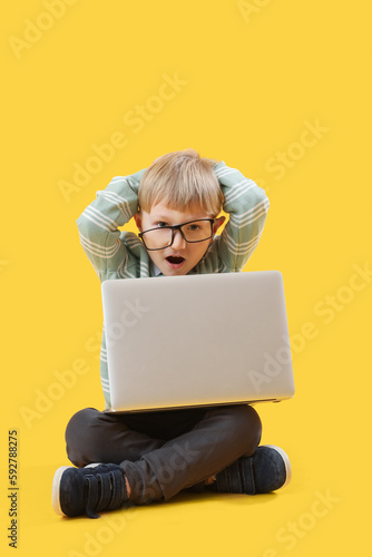 Shocked little businessman with laptop sitting on yellow background