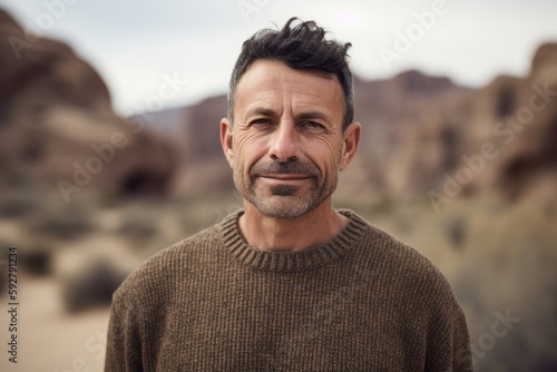 Environmental portrait photography of a pleased man in his 40s wearing a cozy sweater against a canyon or desert landscape background. Generative AI