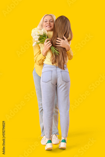Mature woman with tulips hugging her daughter on orange background. Mother's Day celebration