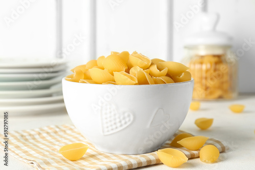 Bowl with raw conchiglie pasta on light background photo