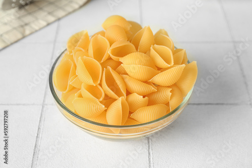 Bowl with raw conchiglie pasta on white tile background photo