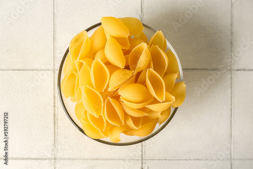 Bowl with raw conchiglie pasta on white tile background photo