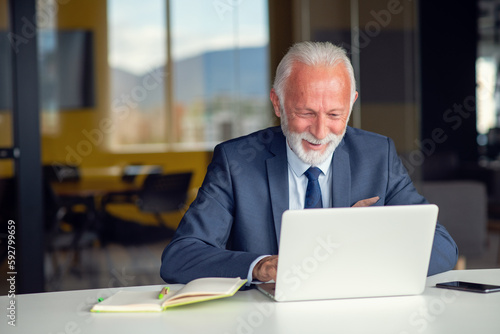 Handsome smiling senior man while sitting at his cozy workplace with laptop at home, retired male chatting with friends in social media, © FS-Stock
