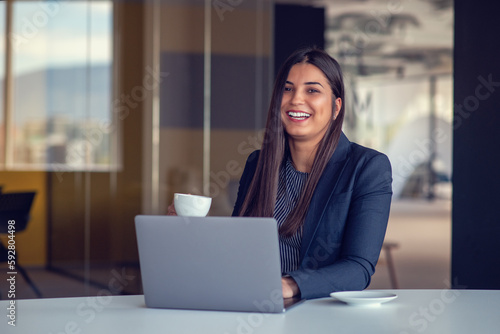 Young woman working on laptop and drinking coffee in office