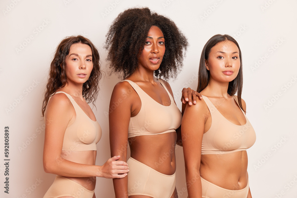 Fotografia do Stock: Three different girls wearing comfortable beige top  and underwear panties stand half-turned inside, one puts her hand on  shoulder of her friend next to, another puts her hand on