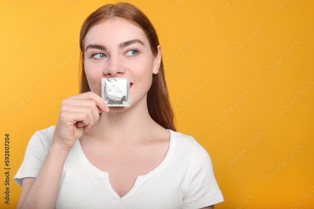 Woman holding condom on yellow background, space for text. Safe sex