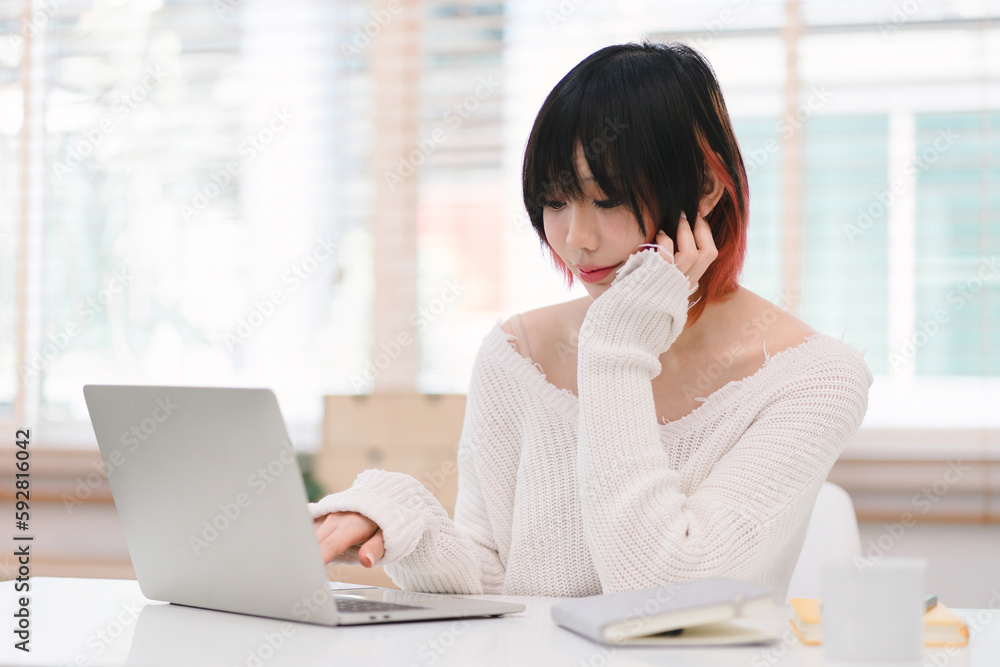 A young Asian female is using her laptop to communicate over the internet from her cozy home office workplace. This depicts the concept of remote work and e-learning. A young Asian female is using her laptop to communicate over the internet from her cozy home office workplace. This depicts the concept of remote work and e-learning.