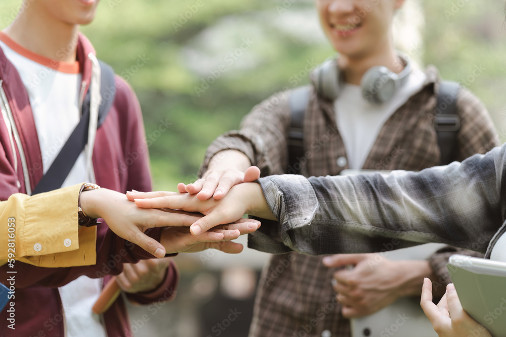 Fototapeta premium A group of diverse, multiracial young people are shown happily stacking their hands together while standing outside a building. This represents a sense of unity, fun,relationship and youth culture.