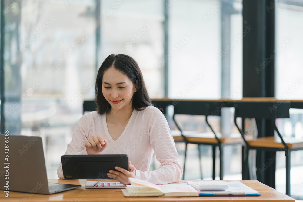 A portrait of a smiling, young, beautiful, professional, and confident millennial Asian businesswoman using a digital tablet to analyze sales data at a co-working space. A portrait of a smiling, young, beautiful, professional, and confident millennial Asian businesswoman using a digital tablet to analyze sales data at a co-working space.