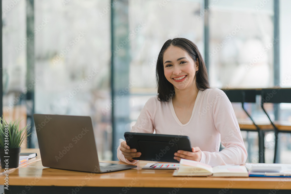 A portrait of a smiling, young, beautiful, professional, and confident millennial Asian businesswoman using a digital tablet to analyze sales data at a co-working space. A portrait of a smiling, young, beautiful, professional, and confident millennial Asian businesswoman using a digital tablet to analyze sales data at a co-working space.
