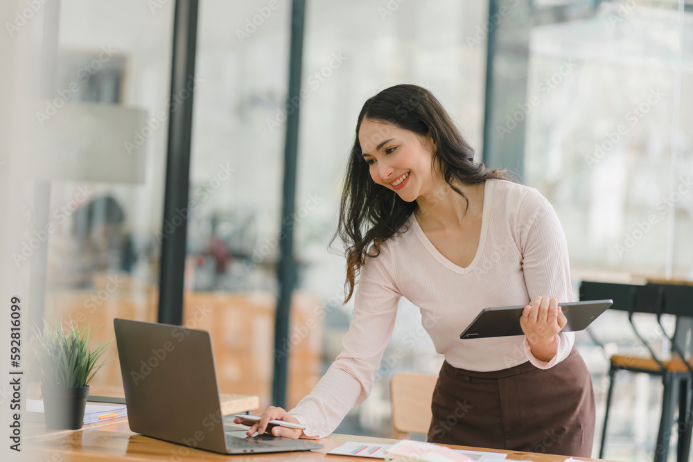 A portrait of a smiling, young, beautiful, professional, and confident millennial Asian businesswoman using a digital tablet to analyze sales data at a co-working space. A portrait of a smiling, young, beautiful, professional, and confident millennial Asian businesswoman using a digital tablet to analyze sales data at a co-working space.