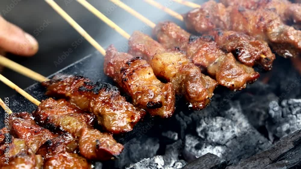 Closeup of beef and chicken satay being barbecue with traditional pit and fired with charcoal, with vendor flipping and fanning the fire Closeup of beef and chicken satay being barbecue with traditional pit and fired with charcoal, with vendor flipping and fanning the fire