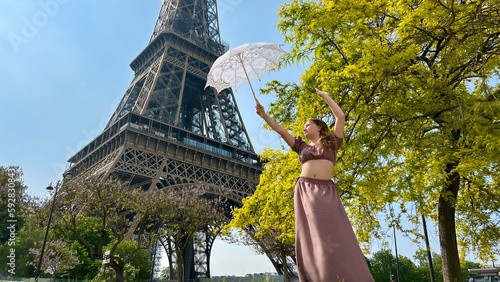 a beautiful young girl dances and spins near the Eiffel Tower with an openwork sun umbrella she is happy rejoices can be used for any advertising for any joy and happiness. High quality 4k footage © Oleksandra